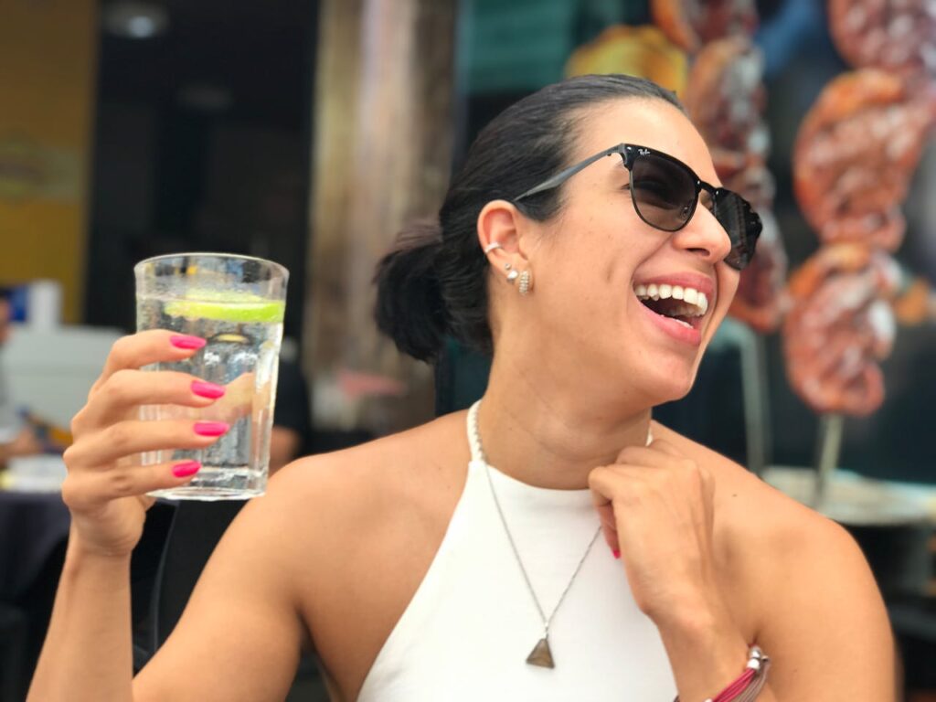 A cheerful woman wearing sunglasses and holding a refreshing drink while enjoying a sunny day.